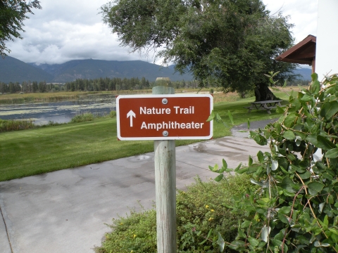 A brown sign points to the Nature Trail Ampitheater. Mountains show in the distance.