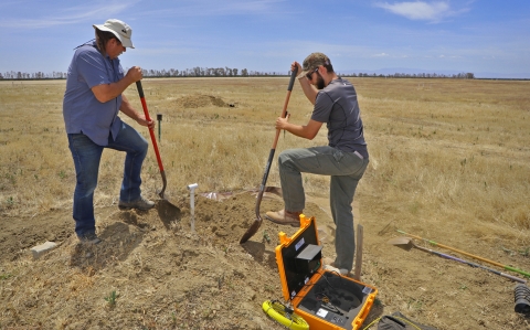 Two men with shovels digging in a field