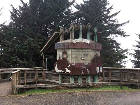 A large wooden walk-in kiosk features copper cut-outs of a lighthouse, trees, and wildlife.