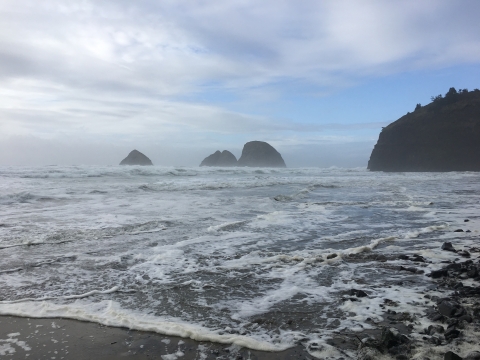 Three islands in the distance, surrounded by a cloud-strewn blue sky and foaming ocean