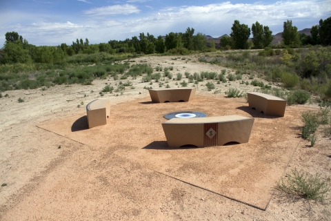 In a desert landscape, four stone benches are arranged around a circle on the ground.