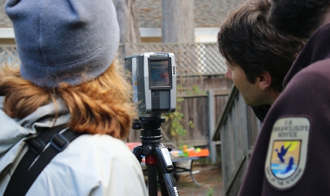 Backs of woman and man standing next to equipment on tripod