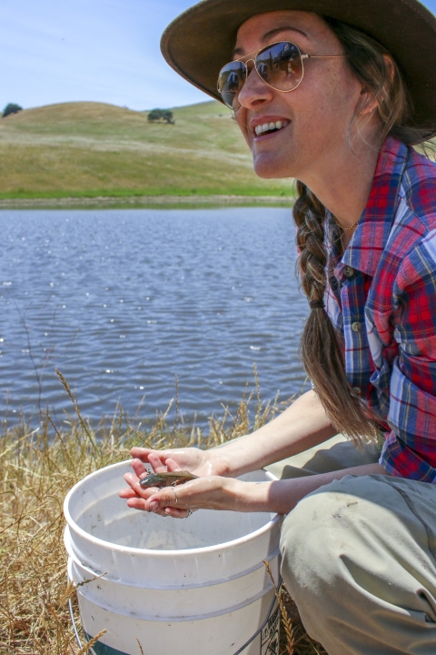 A woman crouches down while holding a salamander in her hands