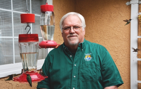 A man wearing a green shirt standing next to two red hummingbird feeders