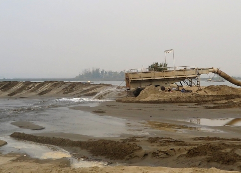 A mix of water and sand is poured from a large piece of equipment onto a sandy, wet area
