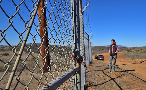 Woman standing outside a fenced in area looking in.
