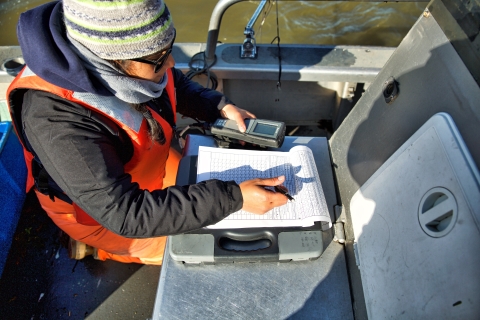 A woman in winter clothing records data on a boat