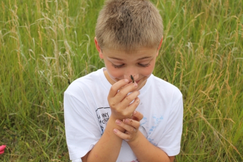 A smiling boy lets a crayfish crawl on his nose