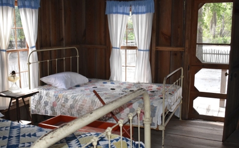  A bedroom with sheer curtains and quilted bedcovers in a wood cabin at Okefenokee National Wildlife Refuge.