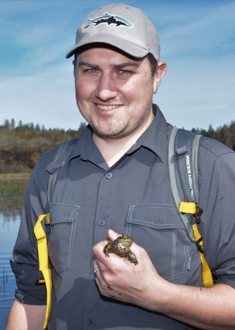 A persons holds a frog in hand. A marsh is in the background.
