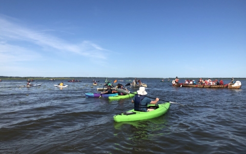 several kayak paddlers on open water near a larger fourteen passenger canoe