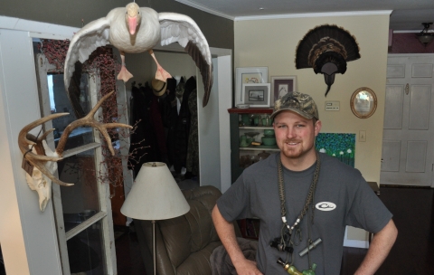 a hunter stands in his living room with a stuffed snow goose above