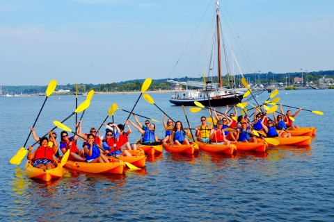 Group of kayakers pose in front of wooden sailboat