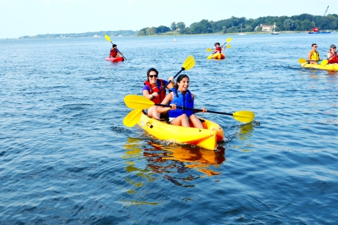 Two smiling girls paddle a yellow kayak across bay