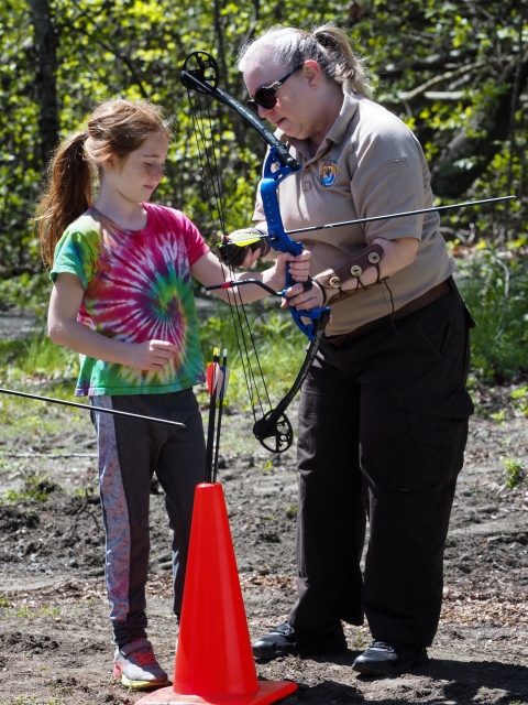 Refuge staff assist a young woman with a compound bow