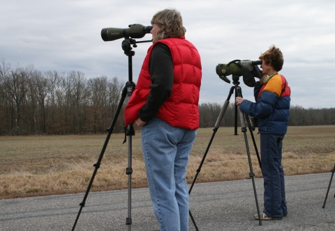 Two people looking through spotting scopes across a field.