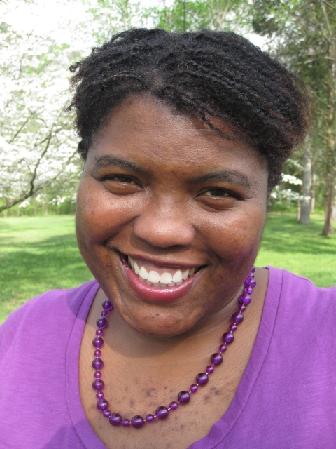 Keena Nichelle Graham smiles, facing the camera, in a tightly framed head-shot image. She wears purple. Grass and trees are visible behind her.