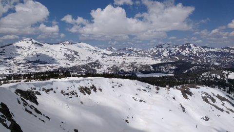 a view of snow-covered jagged mountains against a blue sky dotted with white clouds
