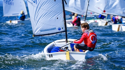 Young boy maneuvers his sailboat across the bay