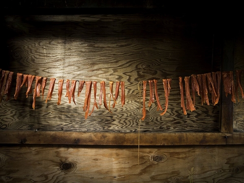 A couple dozen strips of salmon drying on a line in a wooden enclosure