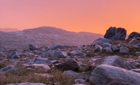 A thunderstorm casts an ominous glow across a rocky landscape.