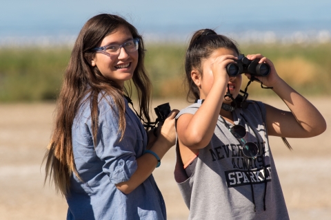 Two young women use binoculars to view birds at Sonny Bono Salton Sea National Wildlife Refuge in California.