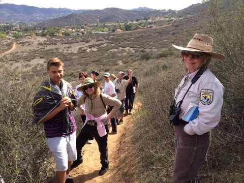 Visitors hike with a ranger in USFWS hat and uniform and wearing binoculars at San Diego National Wildlife Refuge. 