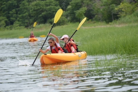 Two young children paddle their kayak through the marsh grasses