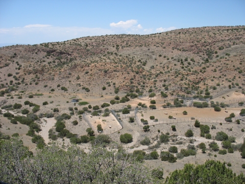A photo looking out onto a desert valley with large fenced enclosures.  There are hills in the background with low vegetation.  