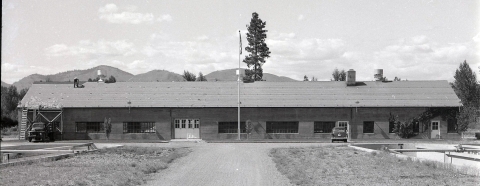 Black and white photo of a long, low building with fish ponds just visible in front on each side of the gravel driveway.