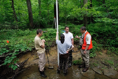 Four people standing in a stream learning how to assess stream condition. 