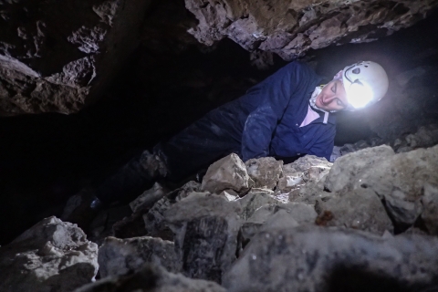 Biologists crawling on her side to get through a narrow passage between a stone floor and stone ceiling in a mine