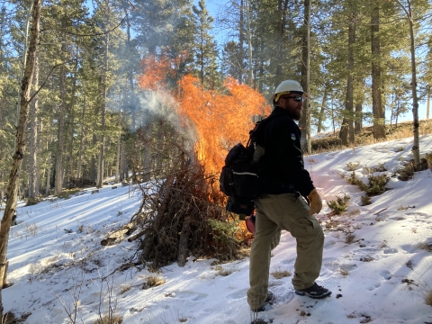 a man walks by a pile of brush on fire in the snowy woods