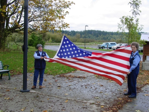 Refuge volunteers Karen Yochem, right, and Barb Sullivan, left, prepare to raise the flag at Billy Frank Jr. Nisqually National Wildlife Refuge in Washington. 