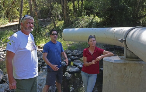 three people outside next to a large steel pipe