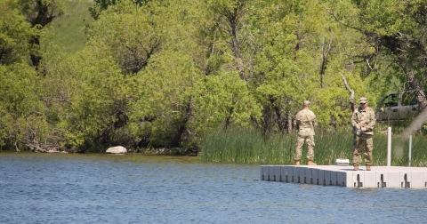 two men in military uniforms fishing from a dock on a lake