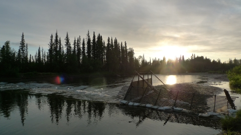 a weir across a river with a low setting sun