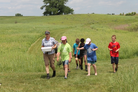 A teacher and 5 students walking on grassy trails in the summer prairie
