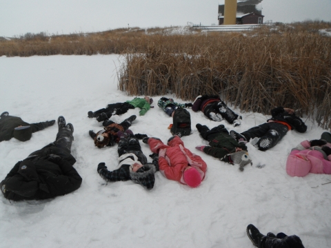 11 children and adults lay on a snowy, frozen wetland
