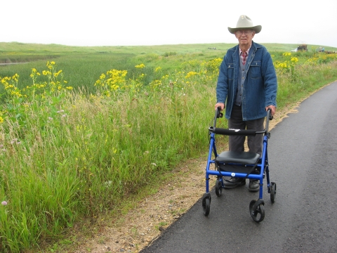 Old many using walker on ashpalt trail in summer prairie
