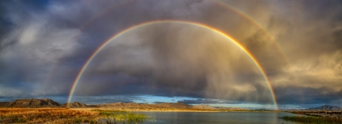 A double rainbow over a spring, mountains in the background, clouds in the sky