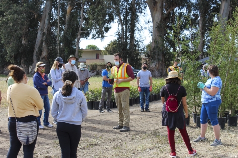 A man wearing a yekkiw vest and face masks addresses a circle of volunteers