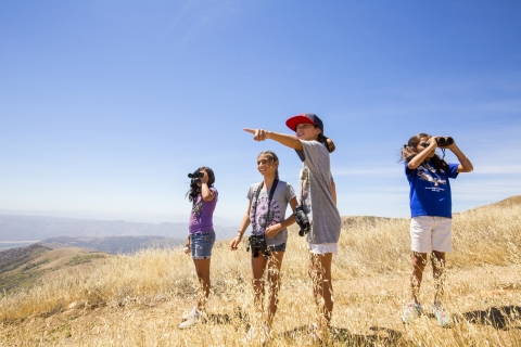 Children searching for condors. Some look through binoculars, another points out. 