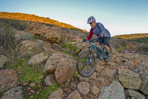 a man on a bike goes over rocks on a trail