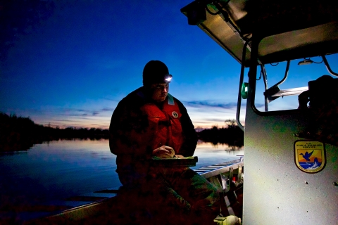 A man on a boat writes on a pad in near darkness