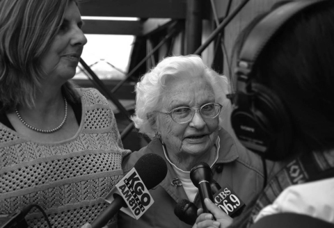 a black and white photo of an elderly woman talking to reporters