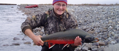 woman holding a bright red fish by a river
