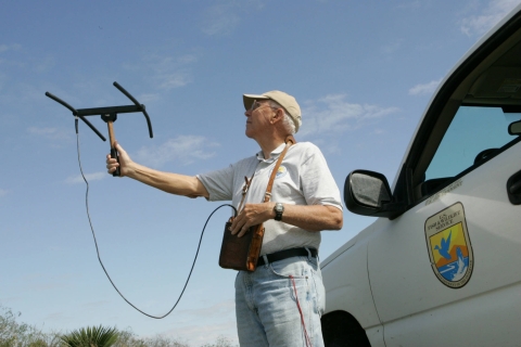 A refuge volunteer holds a radiotelemetry antenna receiver in their hand while standing next to a truck.