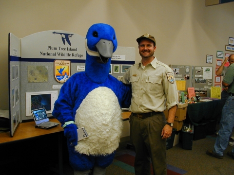 Staff and blue goose mascot in front of outreach board