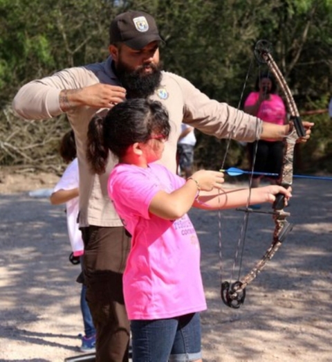 Ranger Garza coaches a girl on proper form while drawing back a bow.